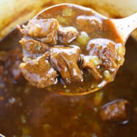 A wooden spoon lifts chunks of beef stew with vegetables from a pot of thick, rich broth—perfect inspiration for anyone learning how to cook beef tips.