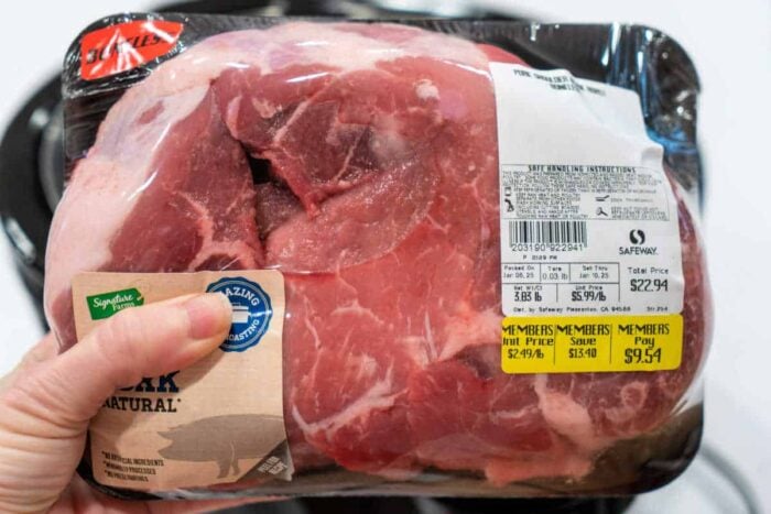 A hand holds a packaged pork shoulder roast with price and weight labels visible on the plastic wrapping—perfect for your next instant pot pork shoulder recipe.