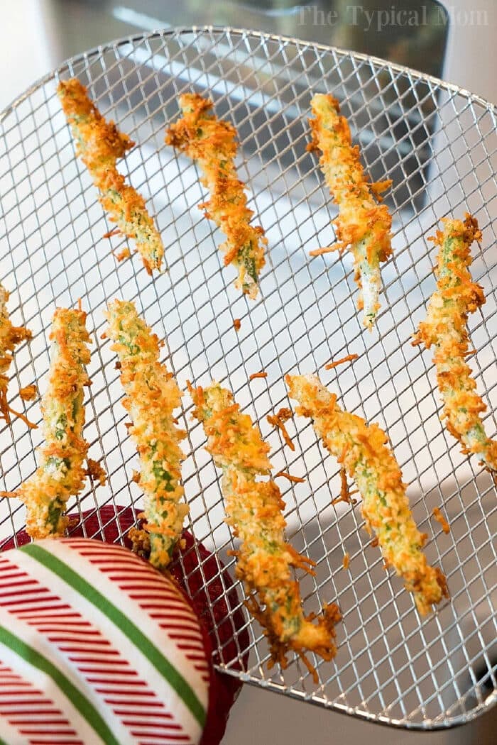 Crispy breaded zucchini fries on an air fryer rack, held with a striped oven mitt&mdash;perfect alongside your favorite Air Fryer Green Bean Fries.