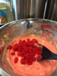 A bowl of pink Maraschino Cherry Bread batter with chopped red cherries being mixed with a black spatula.