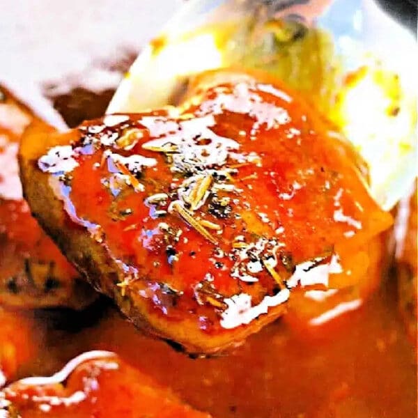 A close-up of a spoon lifting a glazed boneless skinless chicken thigh from the crockpot, covered in sauce and herbs.