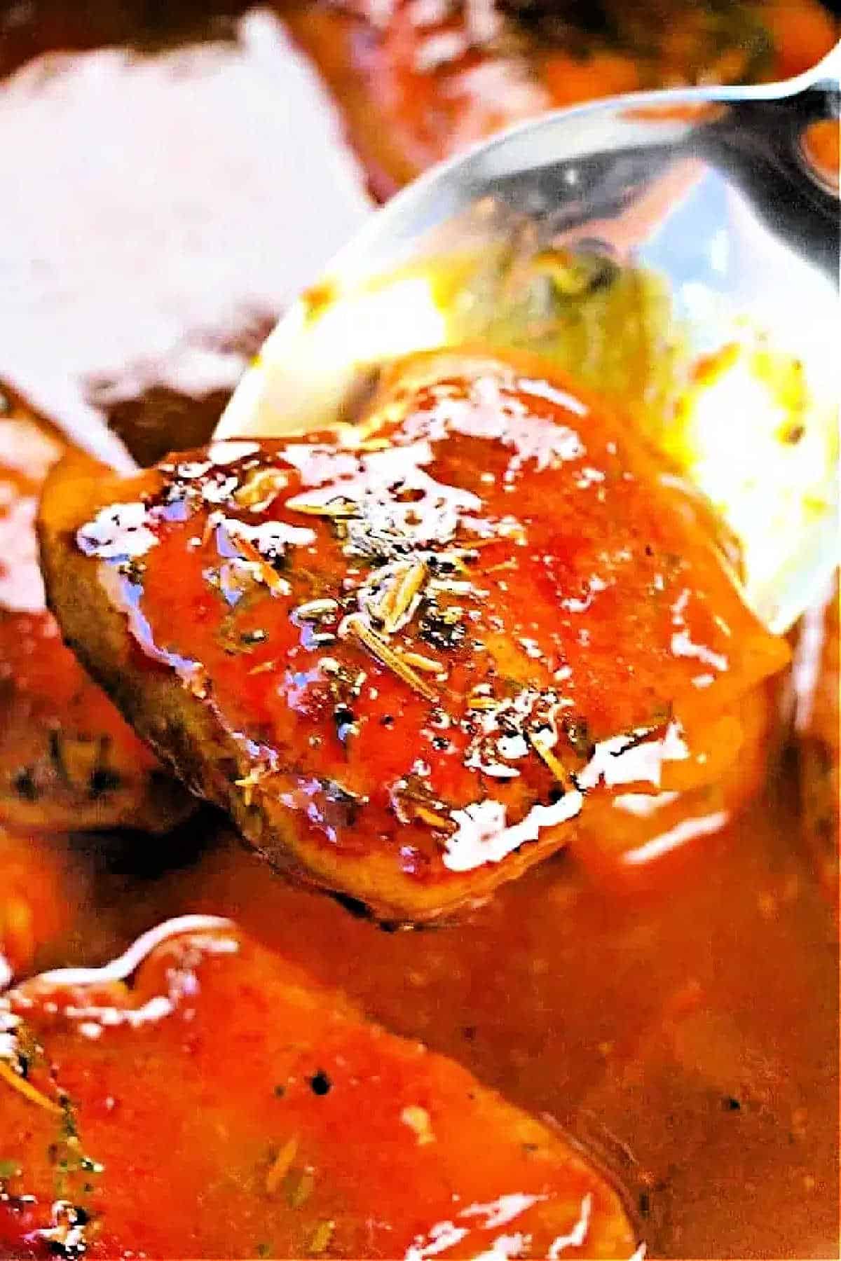A close-up of a spoon lifting a glazed boneless skinless chicken thigh from the crockpot, covered in sauce and herbs.