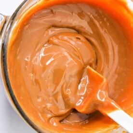 A bowl of melted caramel made from condensed milk is being stirred with a white spatula, showing how to make caramel with condensed milk at home.