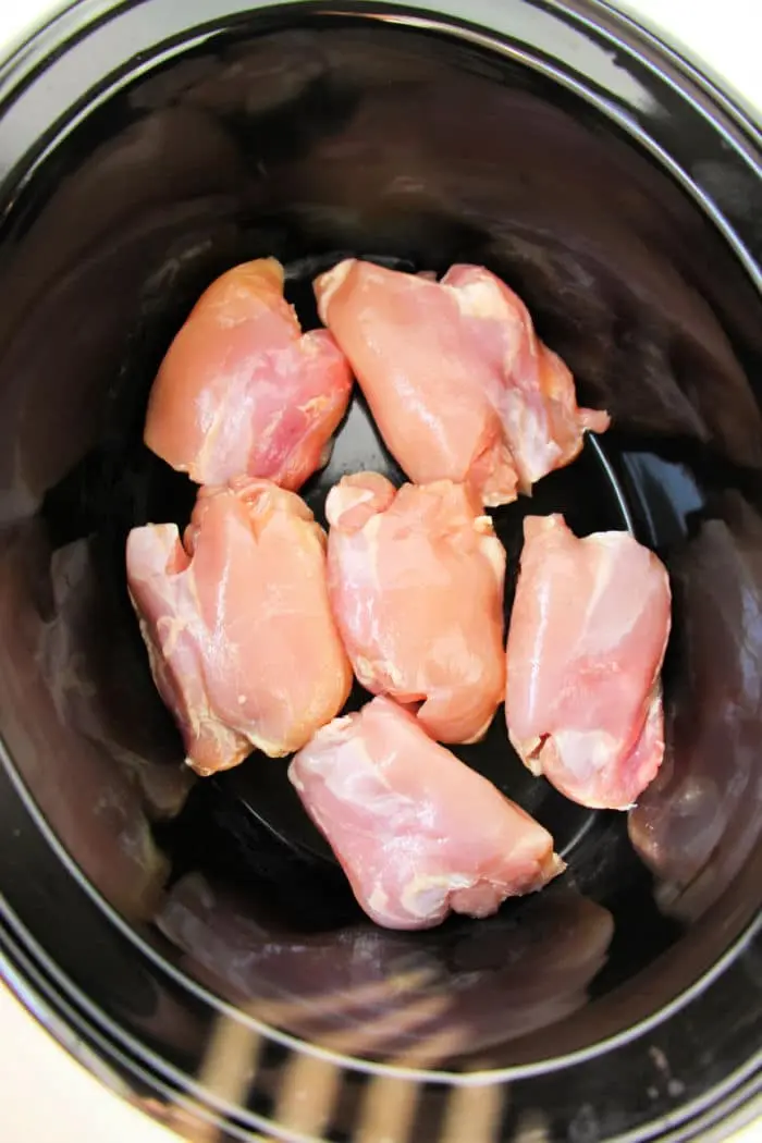 Boneless, skinless chicken thighs nestled in a black crockpot await their transformation into a delicious meal.