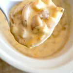 A close-up of a spoonful of creamy mushroom soup, reminiscent of the richness found in crockpot loaded baked potato soup, over a white pot.