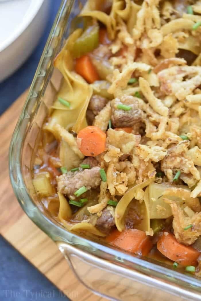 This easy beef stew casserole is comfort food at it's finest!! Packed with tender meat, a thick sauce and lots of vegetables you and your kids are sure to have seconds! Use stew meat or ground beef to make this simple casserole that may become your new family favorite meal. #beef #stew #casserole #easy #vegetable #groundbeef Easy beef stew casserole with carrots, celery, and crispy fried onions in a glass baking dish.