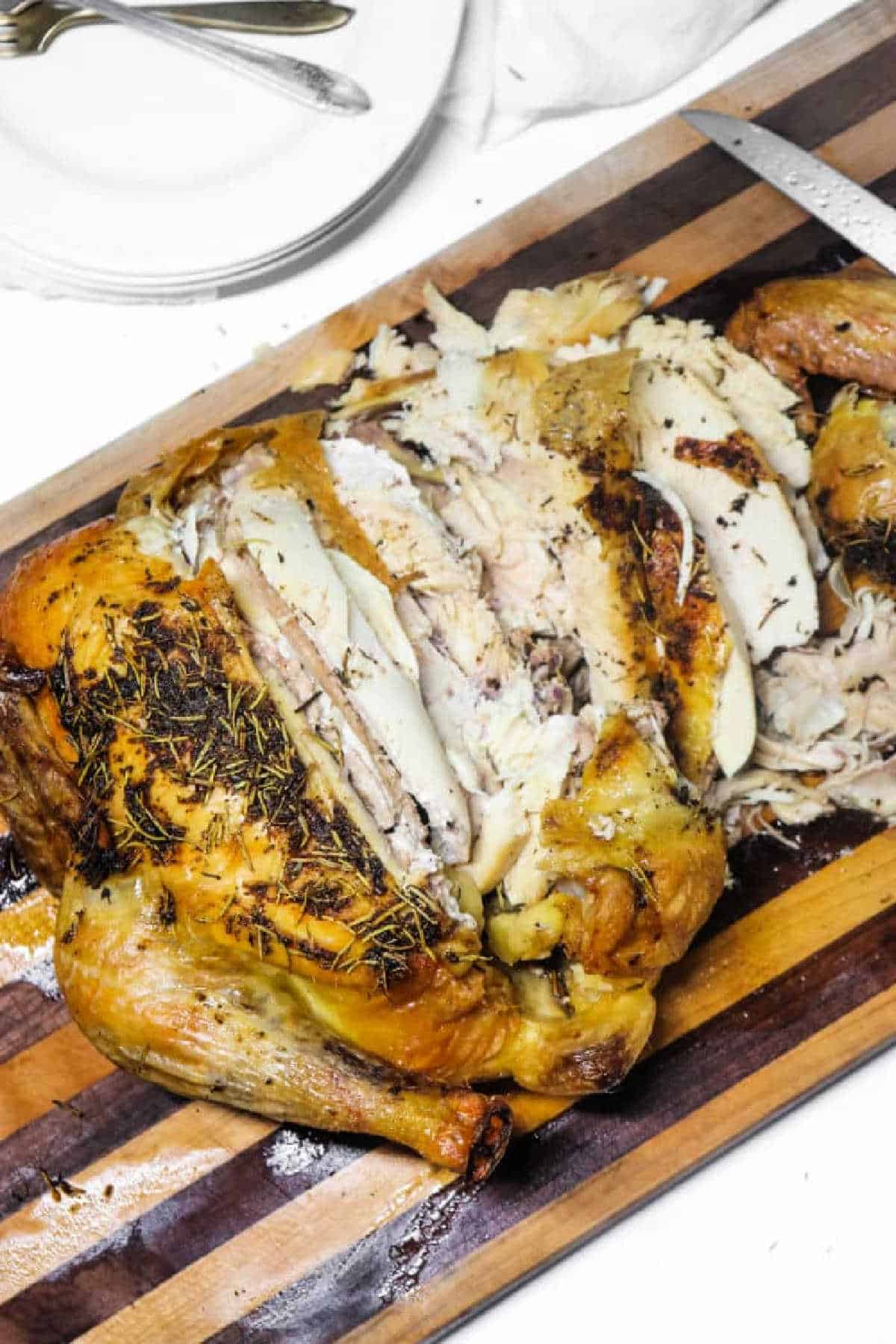 Roast chicken, partially carved, on a striped wooden cutting board with plates and utensils nearby—an inviting scene that suggests the hearty transformation possible even when starting with frozen chicken in oven.