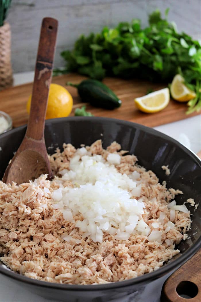 Chopped onions and shredded chicken in a bowl, with a wooden spoon; herbs and lemons in the background—just like you’d gather your ingredients when learning how to make tuna patties, freshness is key for delicious results.