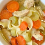 A bowl of Instant Pot chicken noodle soup with carrots, celery, noodles, and tender chicken pieces, served with a spoon inside.