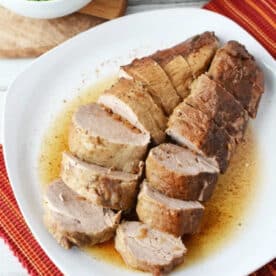 Sliced pork tenderloin cooked from frozen pork loin in Instant Pot, topped with gravy on a white plate, served with mashed potatoes and green peas.