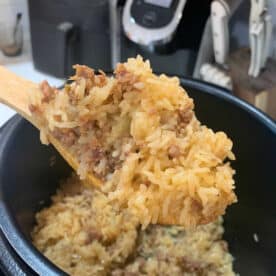 A wooden spoon scoops up instant pot ground beef and rice from a pot, with a kitchen appliance in the background.