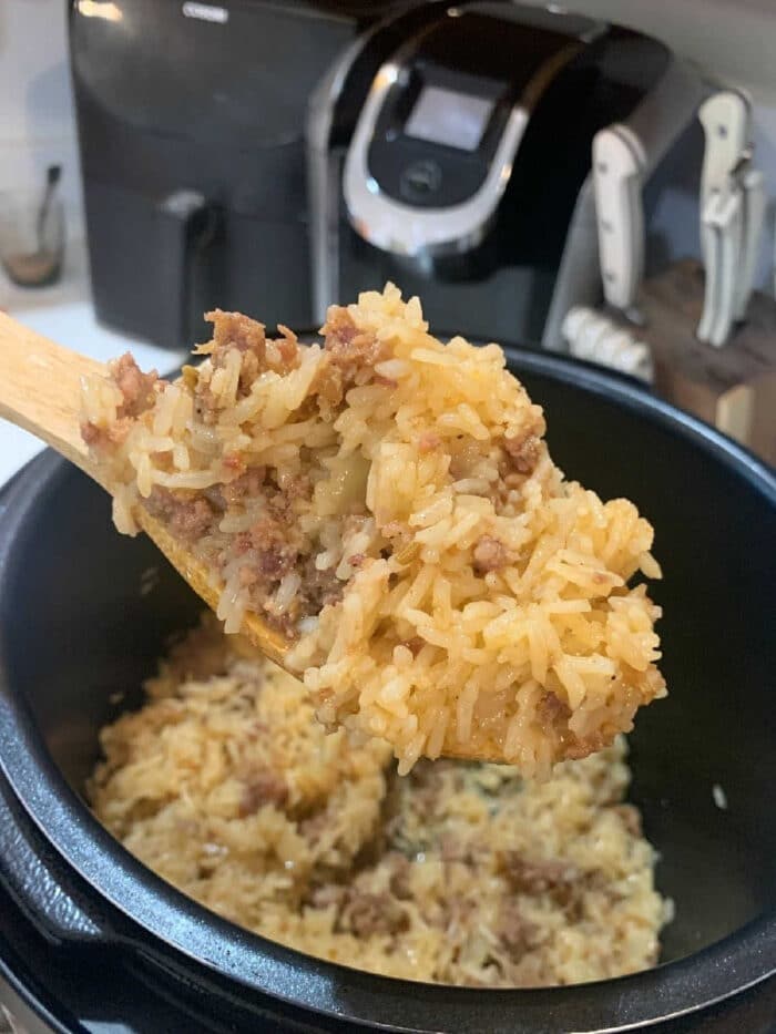 A wooden spoon scoops up instant pot ground beef and rice from a pot, with a kitchen appliance in the background.