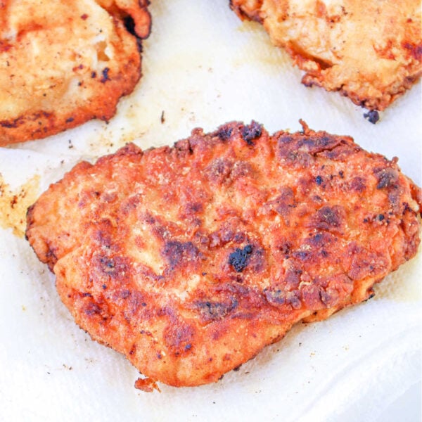 Golden-brown fried chicken pieces, perfectly cooked after learning how long to deep fry chicken breast, drain on white paper towels.
