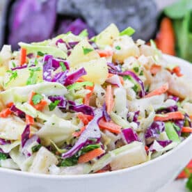 A bowl of colorful Hawaii Coleslaw with green and purple cabbage, carrots, pineapple, and fresh herbs.