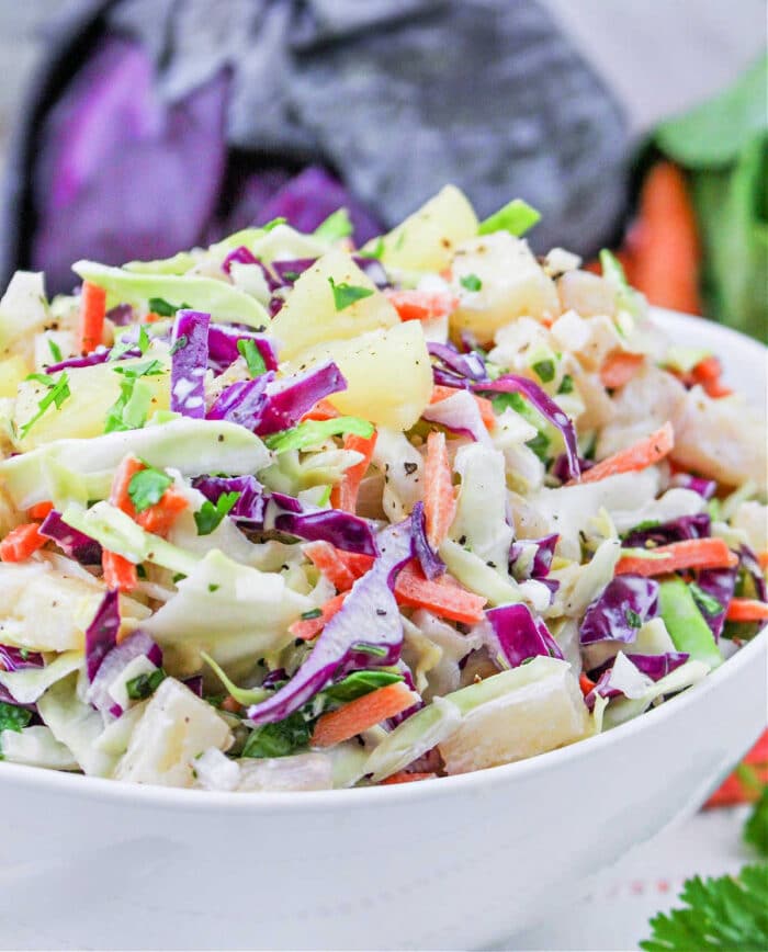 A bowl of colorful Hawaii Coleslaw with green and purple cabbage, carrots, pineapple, and fresh herbs.