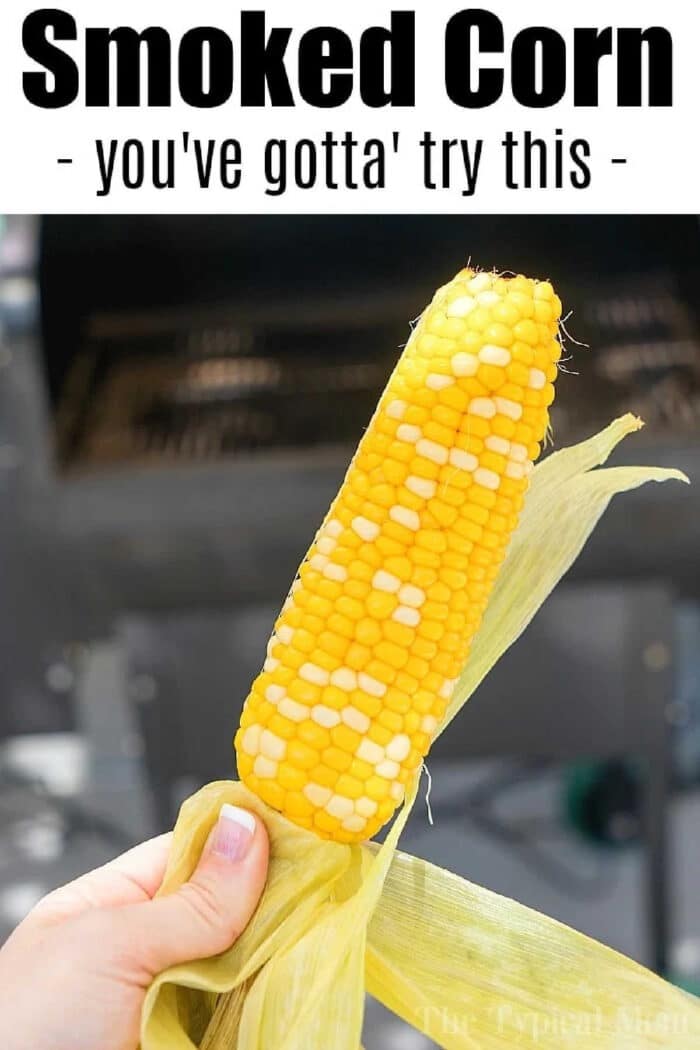 Hand holding a smoked ear of corn with text above that says, Smoked Corn - you've gotta try this. Discover how to smoke corn on the cob for a delicious twist.