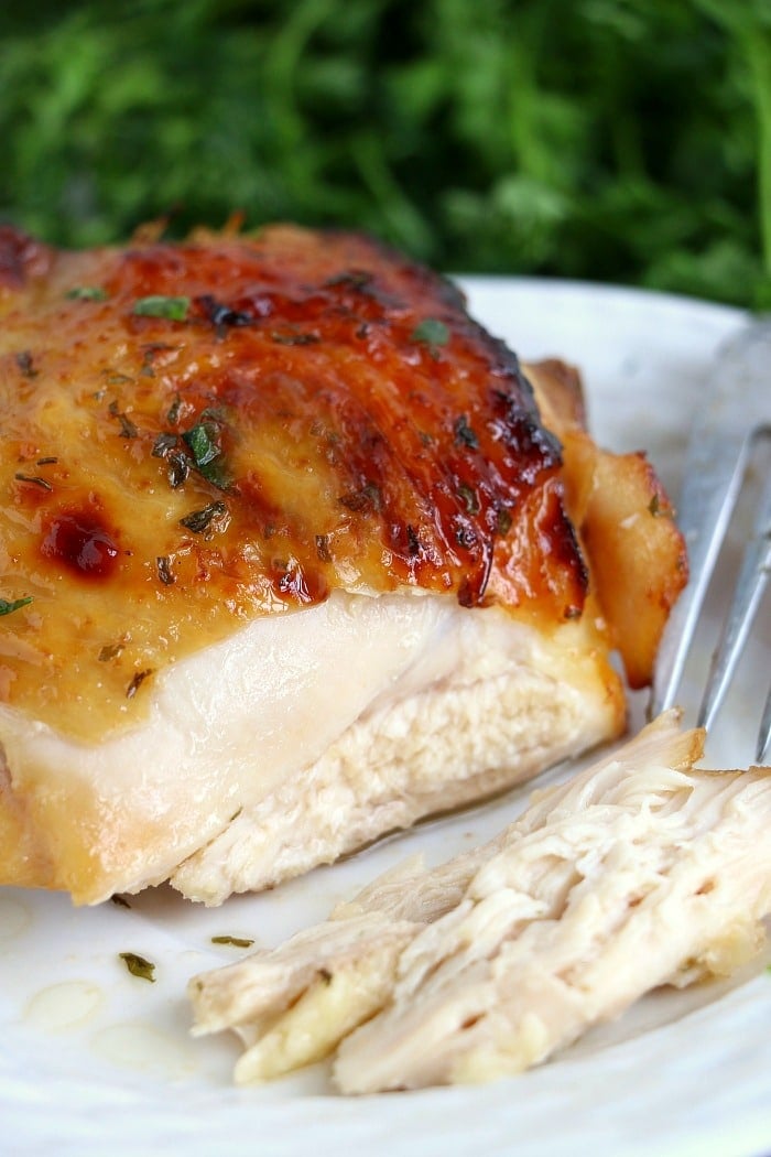 Juicy baked chicken breast with golden, crispy skin on a white plate, reminiscent of marinated chicken in air fryer perfection, with a fork and knife beside it.