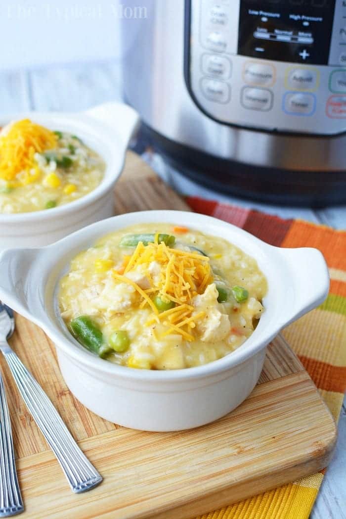 A warm bowl of creamy chicken and vegetable soup made from leftover chicken breast, topped with cheese. An Instant Pot sits in the background, hinting at a convenient approach to delicious leftover chicken breast recipes.