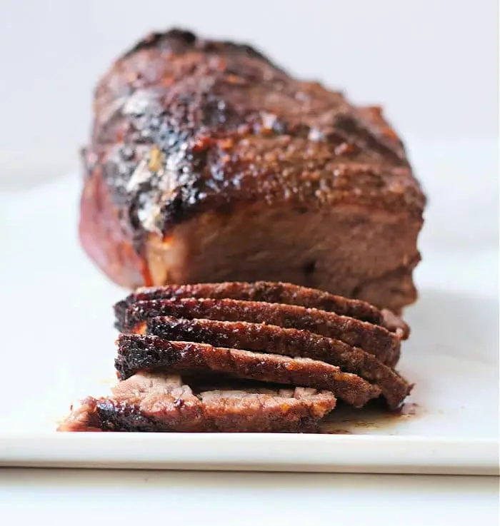 A roasted air fryer roast beef meatloaf placed on a white surface, the meatloaf is browned on the outside. In the foreground, several slices of the meatloaf are cut and displayed.