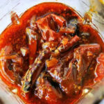 Red chili pickle soaked in oil and spices, with visible whole red chilies and seeds in a glass jar—perfect as a fiery Birria Tacos Sauce or zesty condiment.
