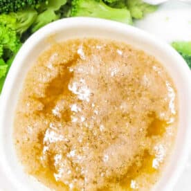 A bowl of Cajun Garlic Butter Sauce next to steamed broccoli florets with a fork.