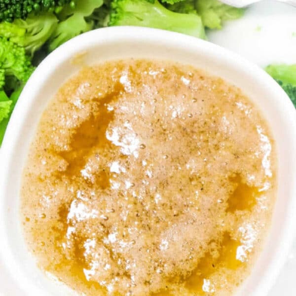 A bowl of Cajun Garlic Butter Sauce next to steamed broccoli florets with a fork.