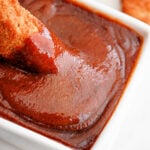 chicken being dipped into rich, popeyes barbecue sauce in a white bowl