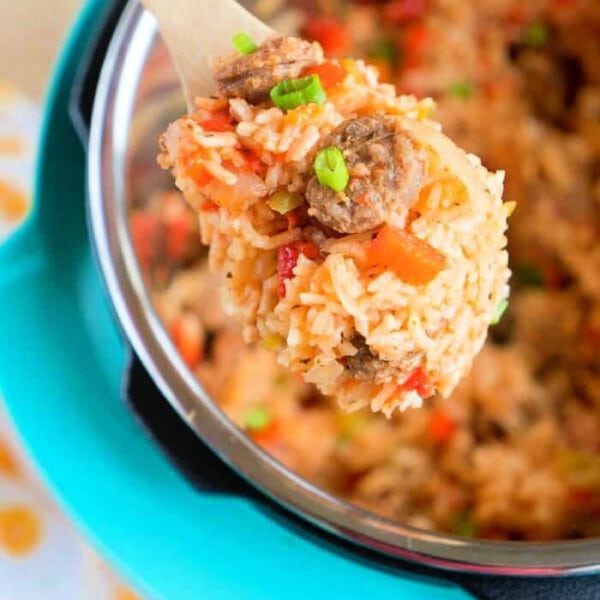 A wooden spoon scoops pressure cooker jambalaya from an Instant Pot, garnished with sliced green onions.