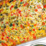 Baked breakfast casserole with sausage, cheese, colorful vegetables, and a hearty queso dip with meat in a foil tray, served next to tortilla chips.