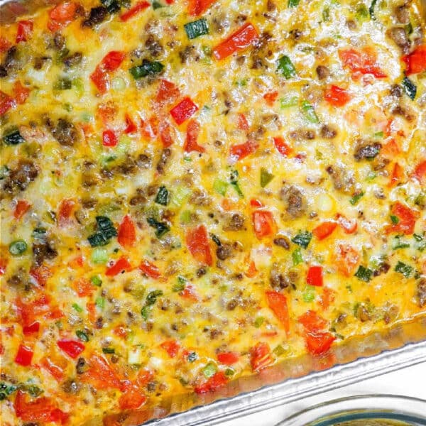 Baked breakfast casserole with sausage, cheese, colorful vegetables, and a hearty queso dip with meat in a foil tray, served next to tortilla chips.