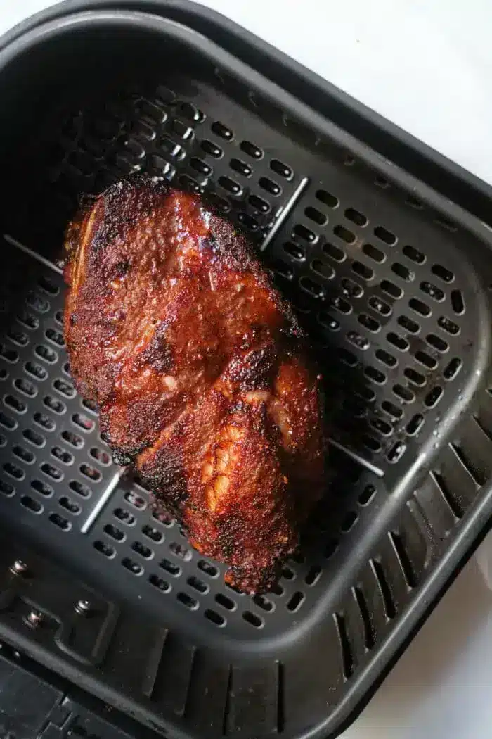 A piece of cooked roast beef with a crispy, charred exterior rests inside a black air fryer basket.