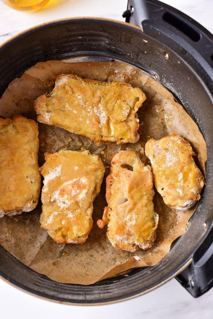 Four pieces of Beer Battered Fish on parchment paper inside an air fryer basket, perfectly crisp and golden from the Air Fryer.