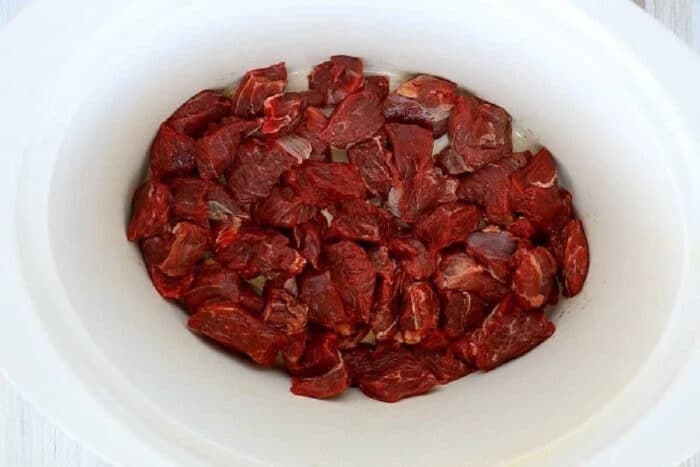 Raw beef chunks arranged in a white slow cooker, perfect for making tender slow cooker beef tips.