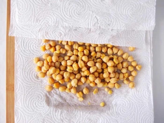 Chickpeas spread on a paper towel, partially covered by another sheet on a wooden surface—perfect prep for making crispy air fryer chickpeas.
