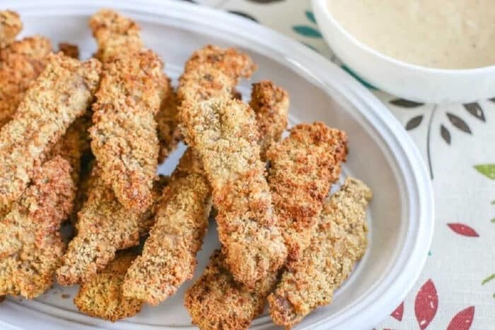 A plate of crispy breaded zucchini fries with a bowl of dipping sauce on the side, served alongside air fryer chicken fried steak for a delicious comfort food combo.