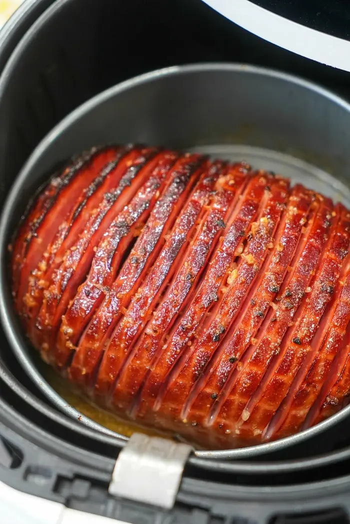 A honey-glazed air fryer ham with a scored surface is shown cooking. The exterior is caramelized to a golden brown with visible seasoning, resting perfectly in the round, black basket.