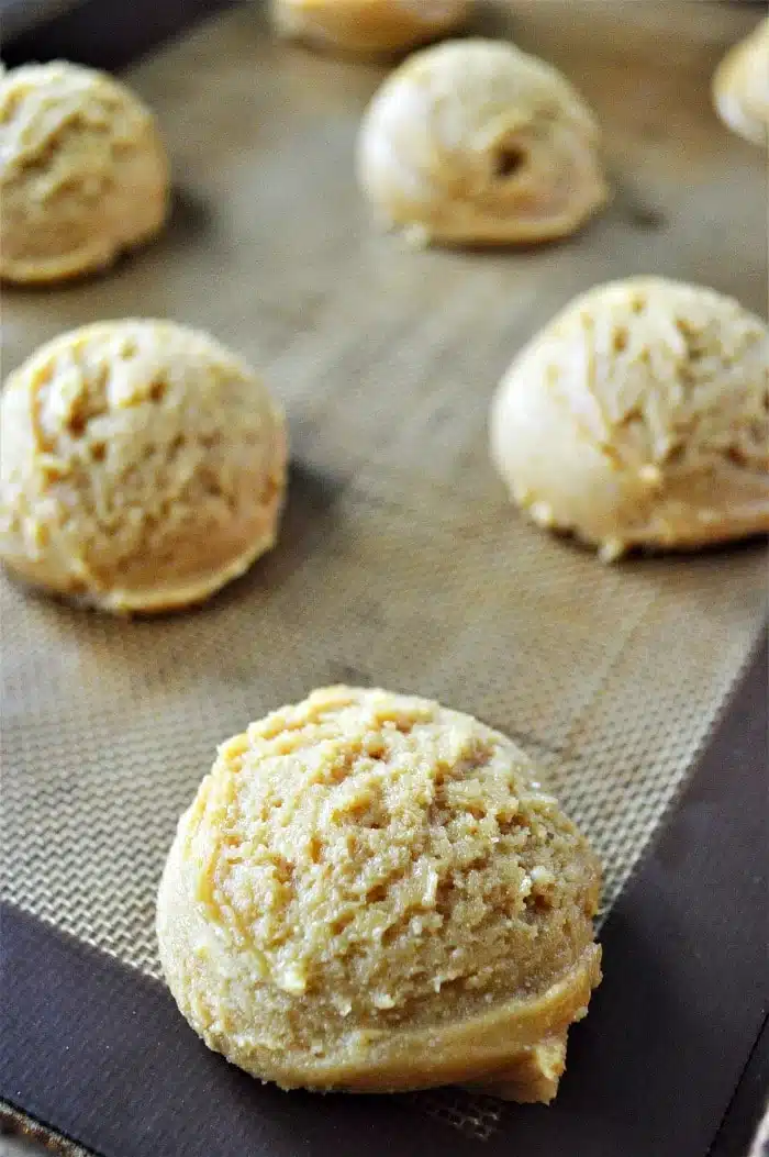 Scoops of raw cookies made with cake mix are spaced out on a baking sheet lined with a silicone baking mat.