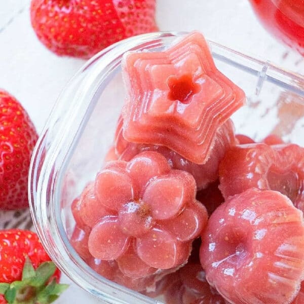 Pink gelatin candies shaped like a star, flower, and bundt, with fresh strawberries nearby—perfect homemade fruit snacks for a delightful treat.