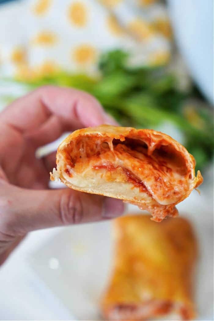 A hand holds a cheesy, sauce-filled pizza roll with a bite taken out of it—just like fresh air fryer hot pockets, crispy on the outside and melty inside.