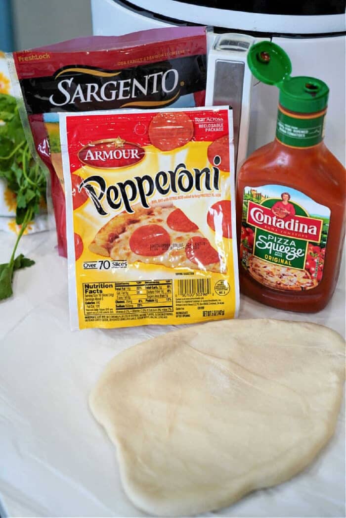 Pizza dough, pepperoni slices, shredded cheese, and pizza sauce are arranged on a kitchen counter, ready to be transformed into homemade air fryer hot pockets.