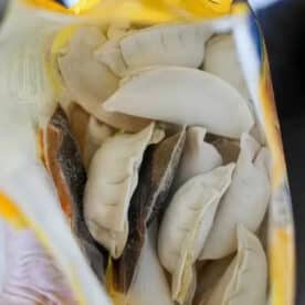 Open bag of frozen dumplings viewed from above, showing several uncooked, crescent-shaped pieces inside—perfect for making potstickers in air fryer.