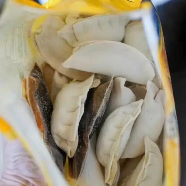 Open bag of frozen dumplings viewed from above, showing several uncooked, crescent-shaped pieces inside—perfect for making potstickers in air fryer.