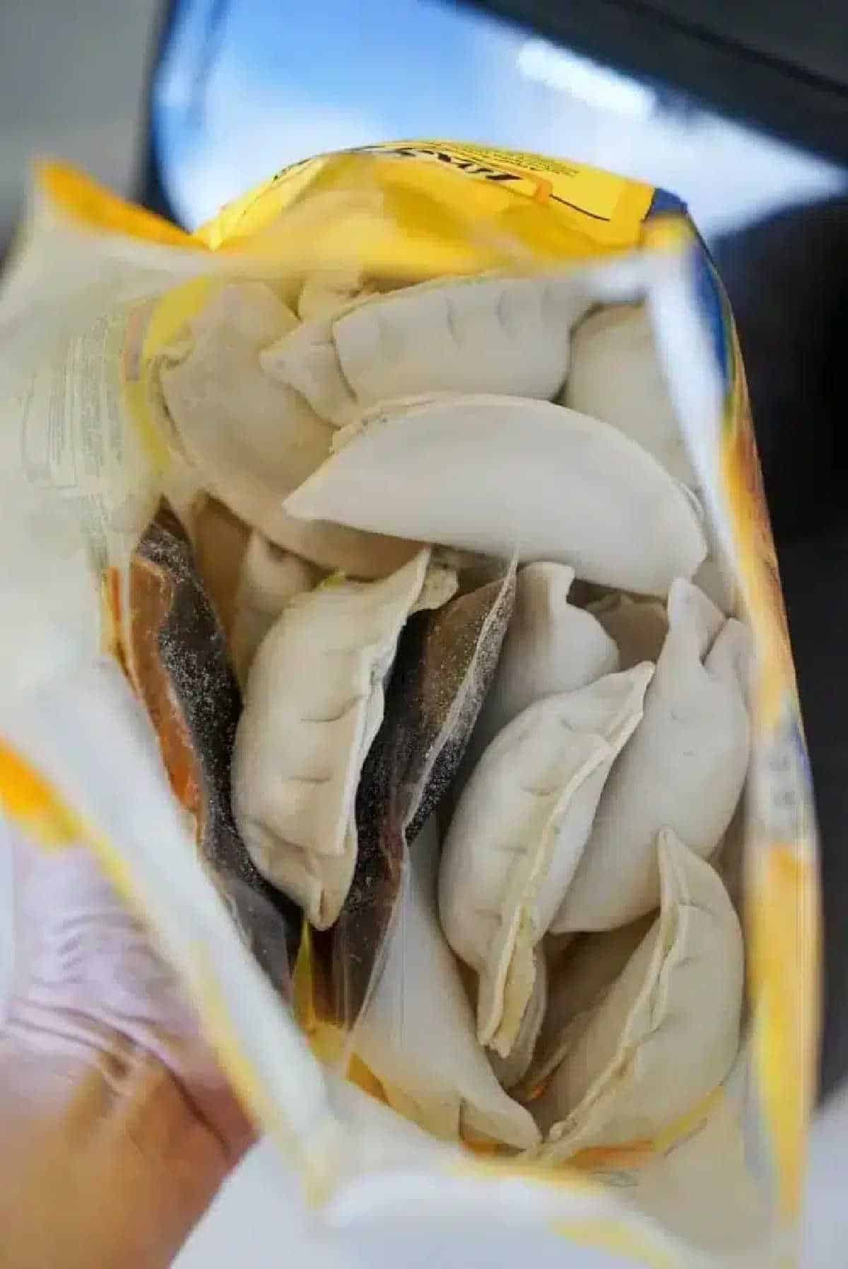 Open bag of frozen dumplings viewed from above, showing several uncooked, crescent-shaped pieces inside—perfect for making potstickers in air fryer.