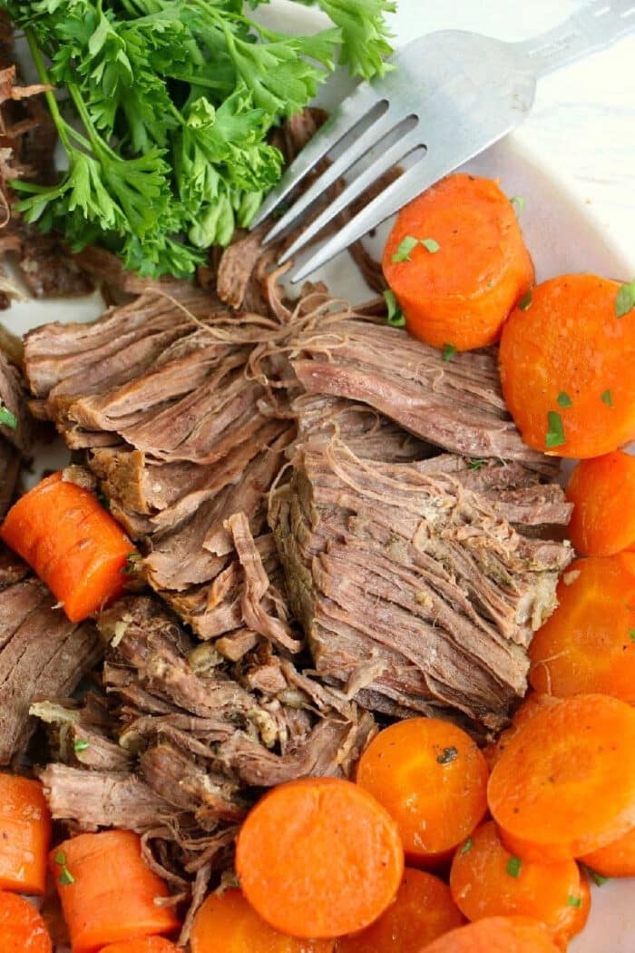 Shredded pot roast with cooked carrots and fresh parsley, prepared from a frozen roast in the Instant Pot, with a fork resting near the meat.