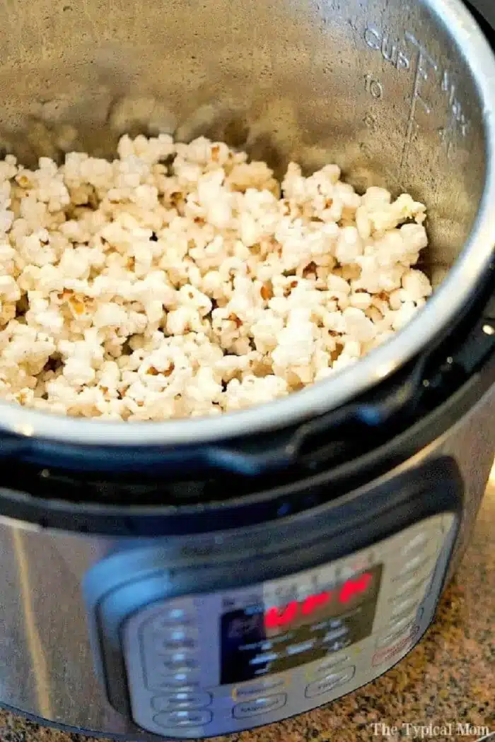 The Instant Pot is filled with a mountain of popcorn, its gleaming metallic interior adding a modern twist to this classic snack. The digital control panel stands out, while the brown and tan speckled countertop beneath exudes a cozy charm.