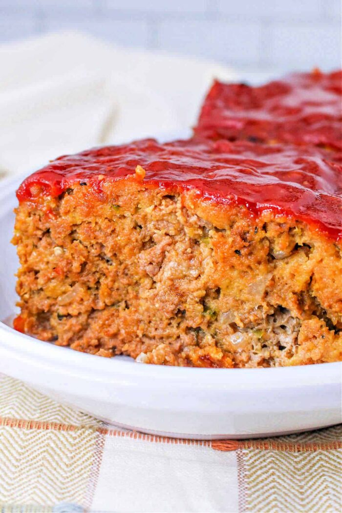 A close-up of homemade meatloaf with a glossy red ketchup glaze—try swapping it with How to Make Sweet Baby Rays Honey BBQ Sauce for a sweet and tangy twist—served on a white plate.