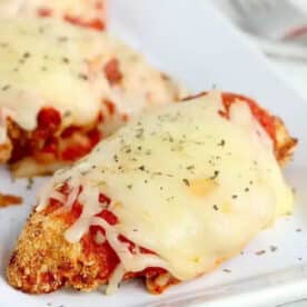 Air fryer chicken parm topped with melted cheese and herbs on a white plate.