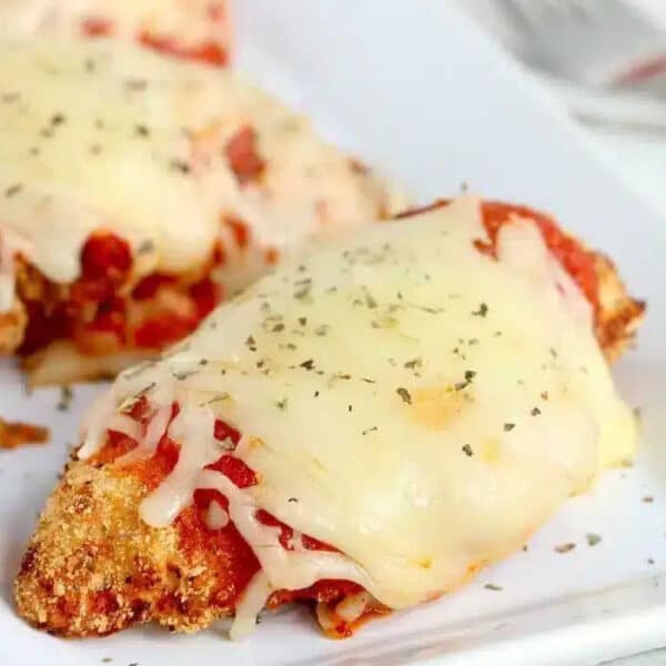 Air fryer chicken parm topped with melted cheese and herbs on a white plate.