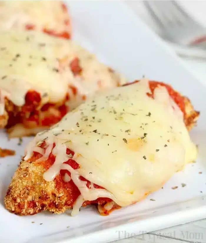 Air fryer chicken parm topped with melted cheese and herbs on a white plate.