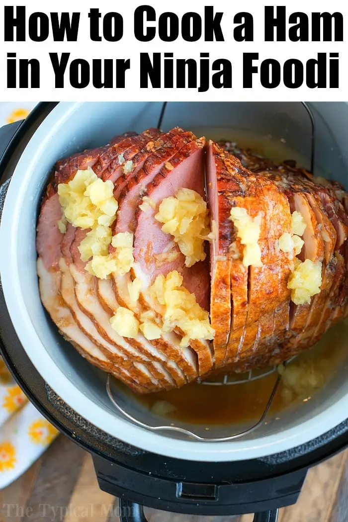 A sliced ham topped with a pineapple glaze is shown inside a Ninja Foodi cooker. The text "How to Cook an Air Fryer Ham in Your Ninja Foodi" is displayed at the top of the image.